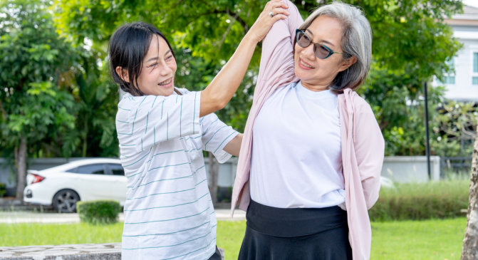 elderly woman doing body stretch with the assistance of her caregiver